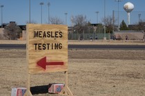 A wooden sign reads "MEASLES TESTING" and has an arrow pointing to the left