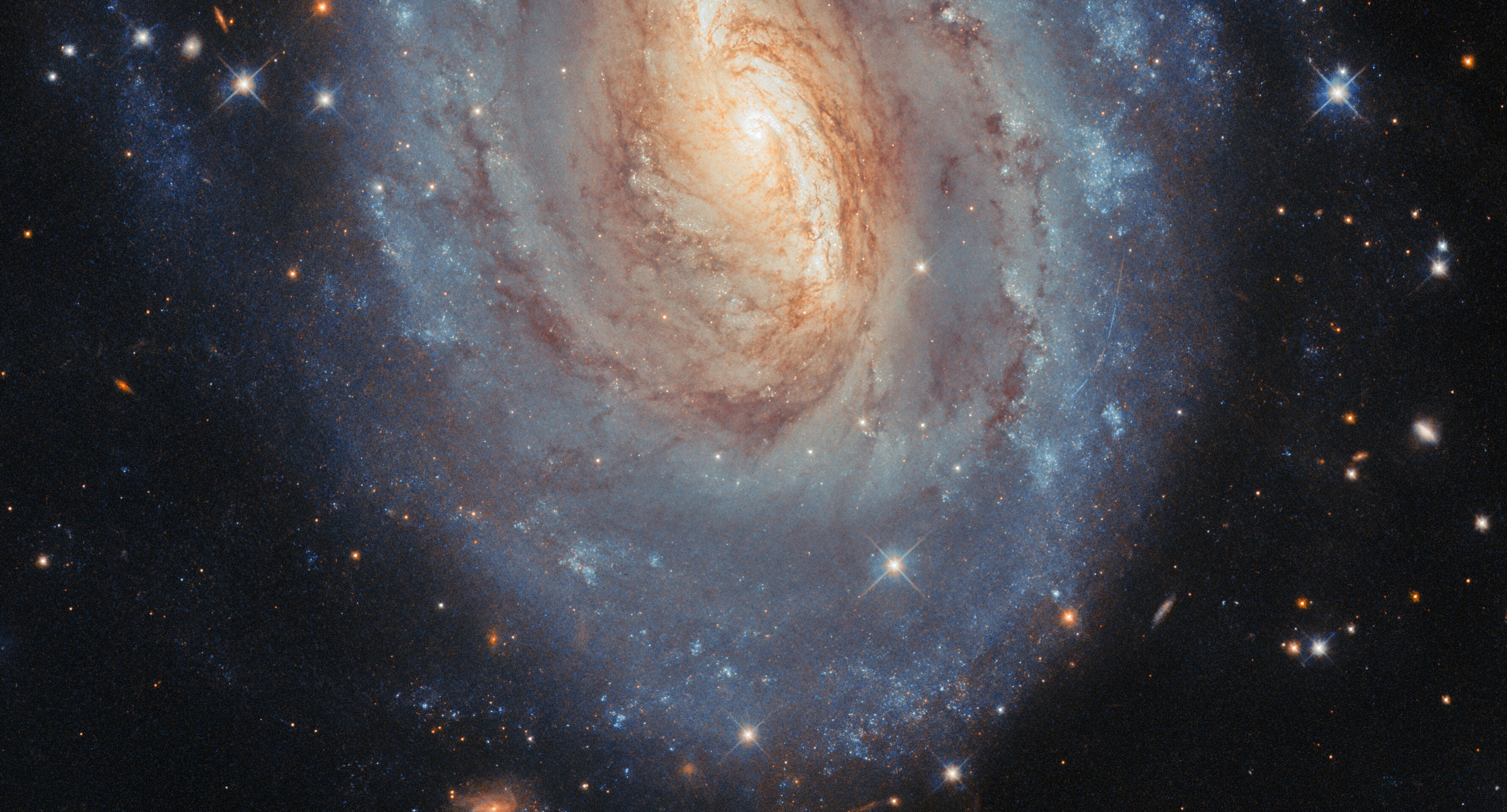A telescopic view of a distant spiral galaxy with a yellowish center and more blue-colored star-forming regions toward the outer regions.