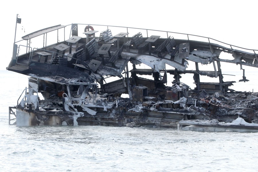 A completely burned sightseeing boat floats in water.