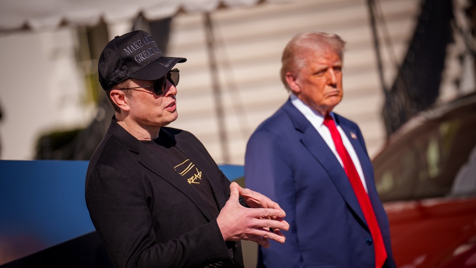 Elon Musk clasps his hands standing next to Donald Trump