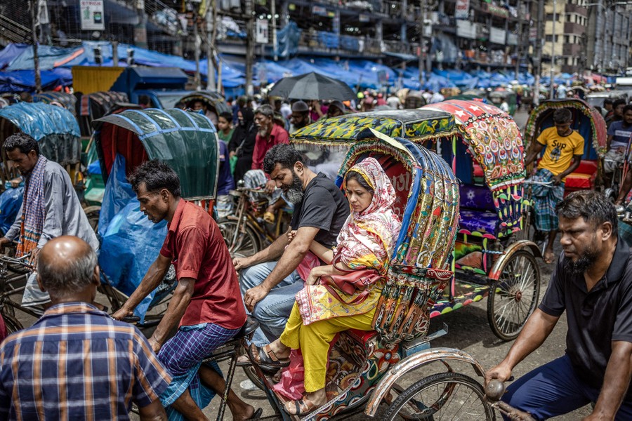 Many people fill a busy street on foot and in rickshaws.