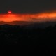 An aerial image showing vehicles driving on a freeway as the sun sets behind smoke from wildfires in Los Angeles