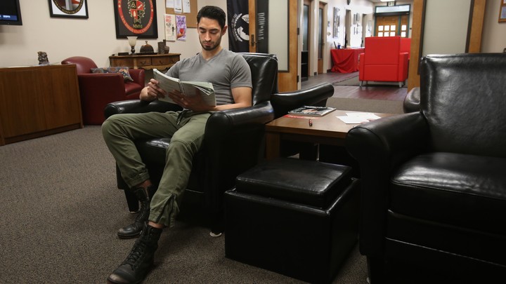 A man sits in a leather chair reading a textbook.