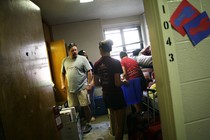 A family unpacks a student's luggage and furniture in a dorm room. 