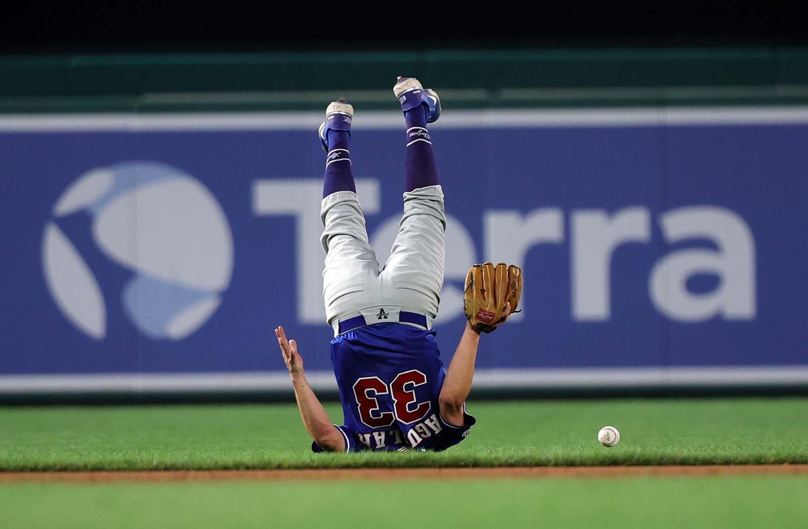 A person wearing a baseball uniform, upside down, tumbling after a ball