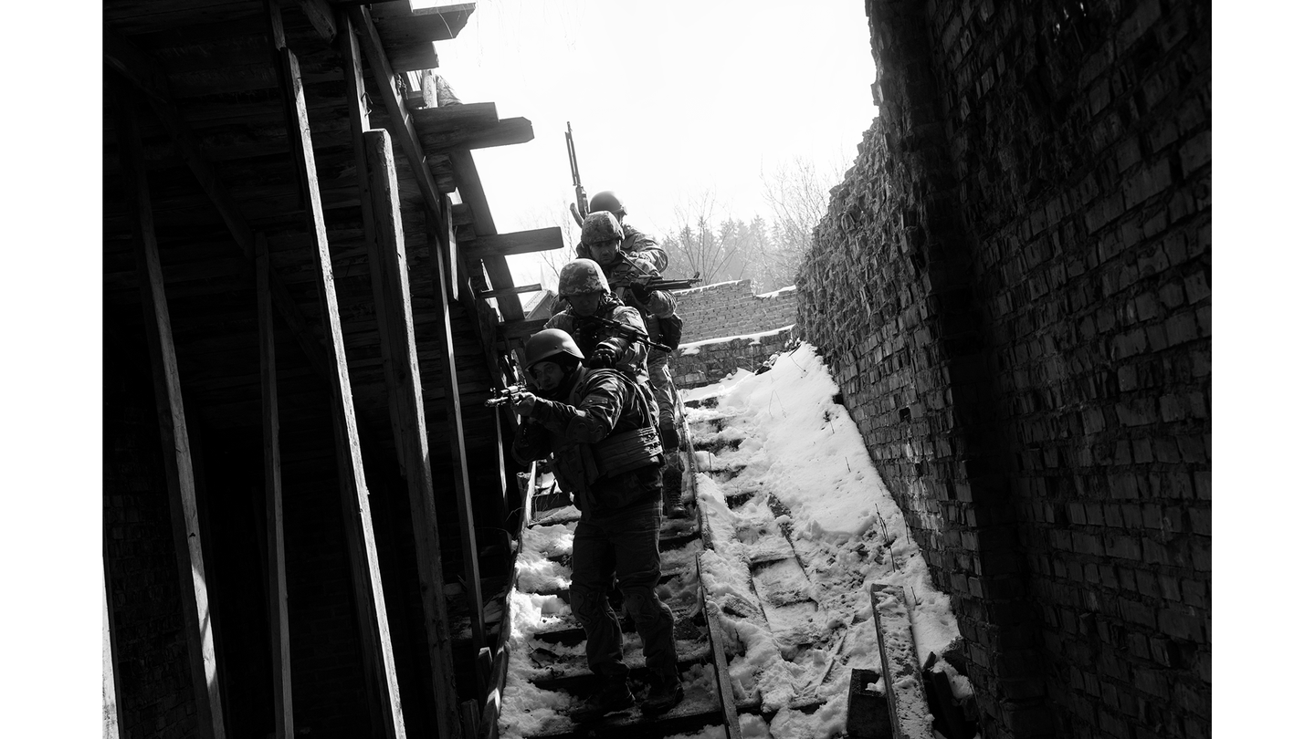 black-and-white photo of soldiers aiming weapons, descending open staircase in snow with sky behind