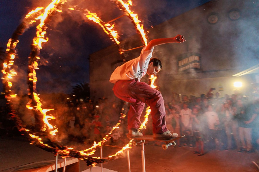 A person on a skateboard jumps through a flaming hoop.