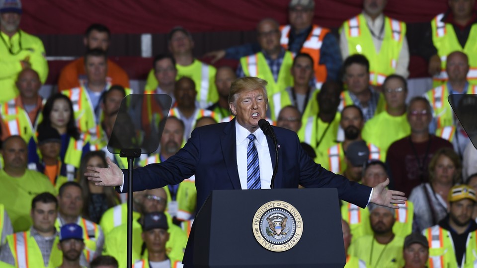 Trump gives a speech in front of workers wearing yellow vests.