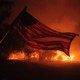 An American flag waves in front of a wildfire.