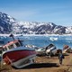 A man walks among boats with snow-covered mountains in the distance.