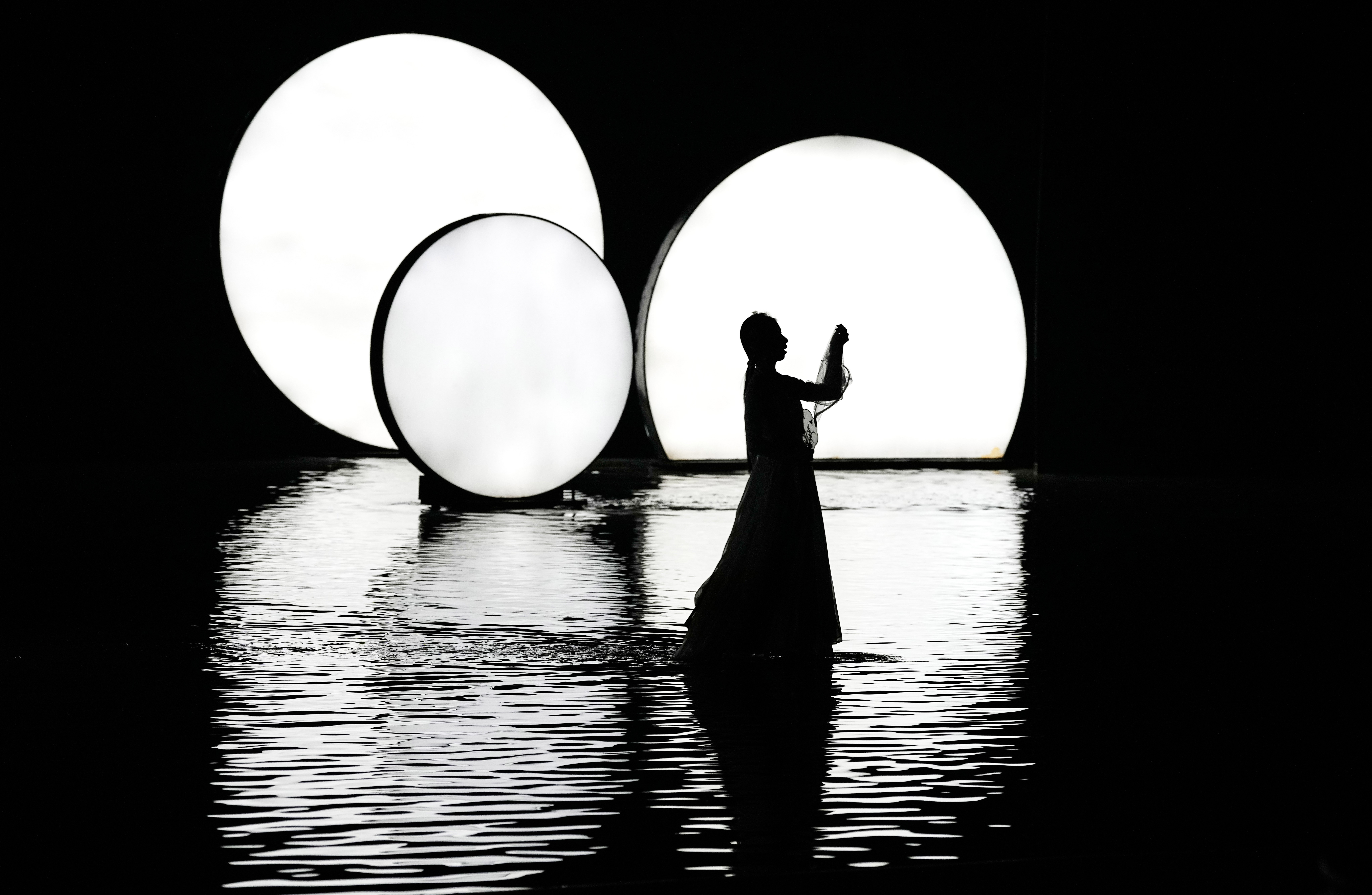 An actress is silhouetted as she performs on a water stage.