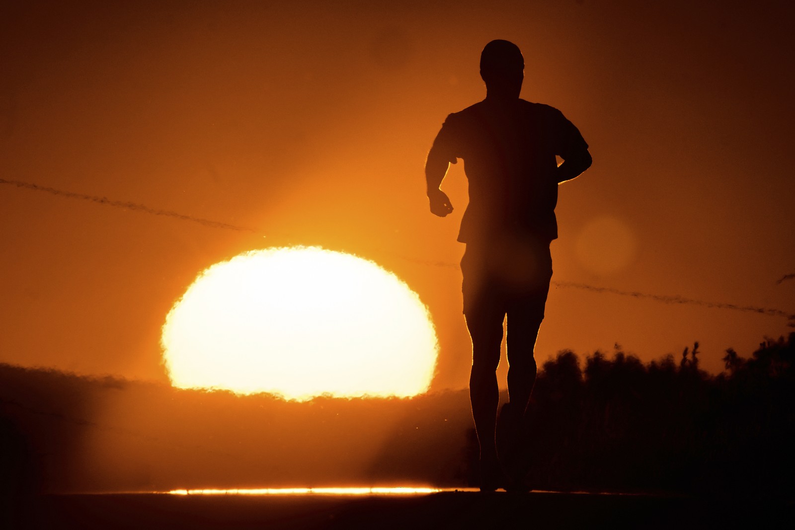 A man runs, backdropped by the sun on the horizon.