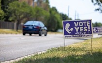 Car driving past a sign that reads "vote yes!"