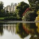 A photograph of a castle in the distance while foliage reflects in a closer still lake