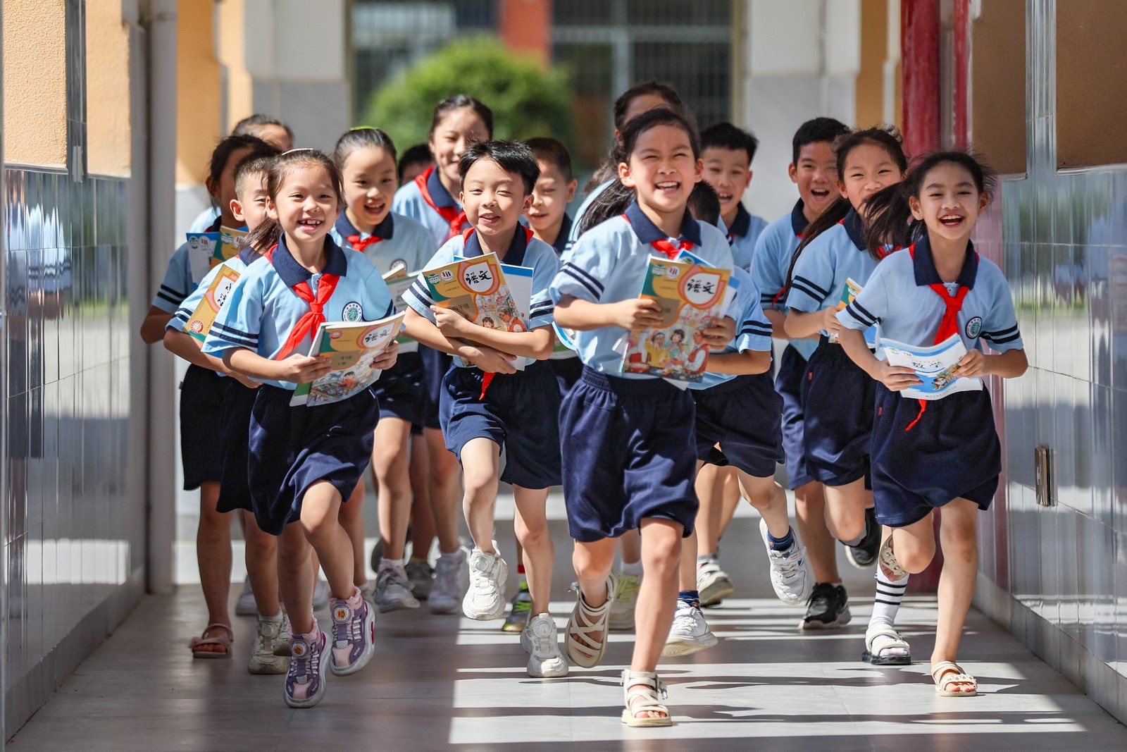Young students wearing school uniforms smile and run along a hallway.