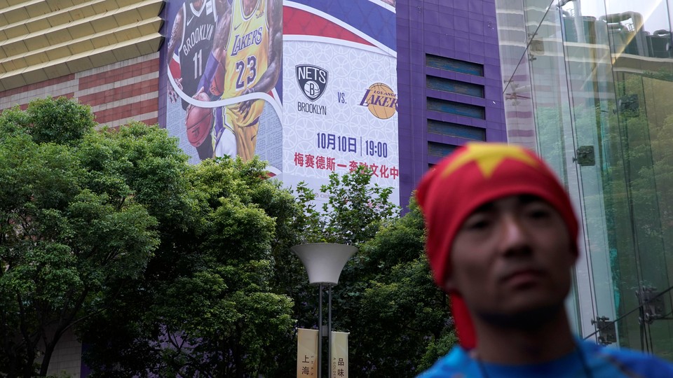 A man with his head wrapped in a Chinese national flag is seen near a building with a partly removed banner advertising an NBA game in Shanghai.