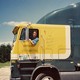 A man leans out of the window of a large truck with a blue and yellow cab.