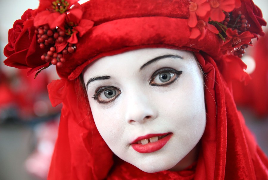 A close view of a young protester wearing a red head covering and white face makeup.