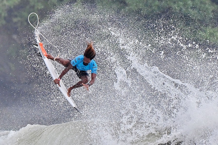A surfer grabs his board while jumping off a wave.