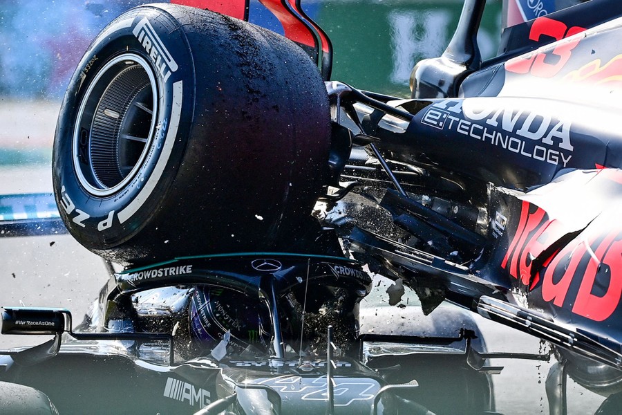 Two Formula One race cars collide, with one riding atop the other, its rear tire hitting dangerously close to the other driver's head.