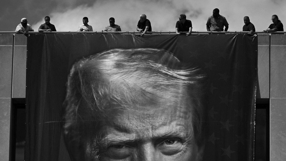 Black and white photograph of workers hanging an enormous banner of Trump's face on the facade of the Department of Labor building