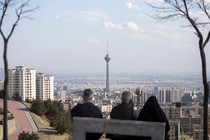 Photograph taken from behind of three figures on a bench overlooking Tehran's skyline.