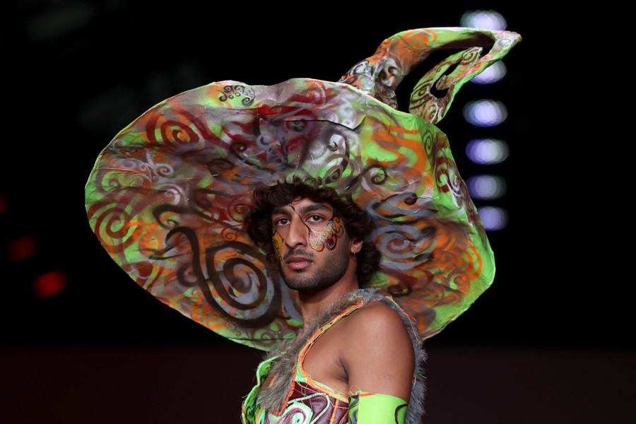 A model wears a large stylized hat on a runway.