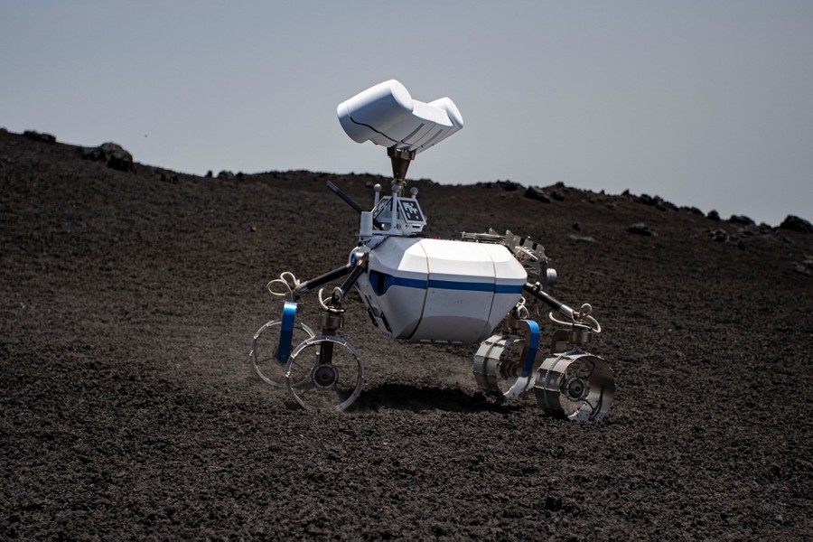 A small four-wheeled robot rolls across a volcanic slope.