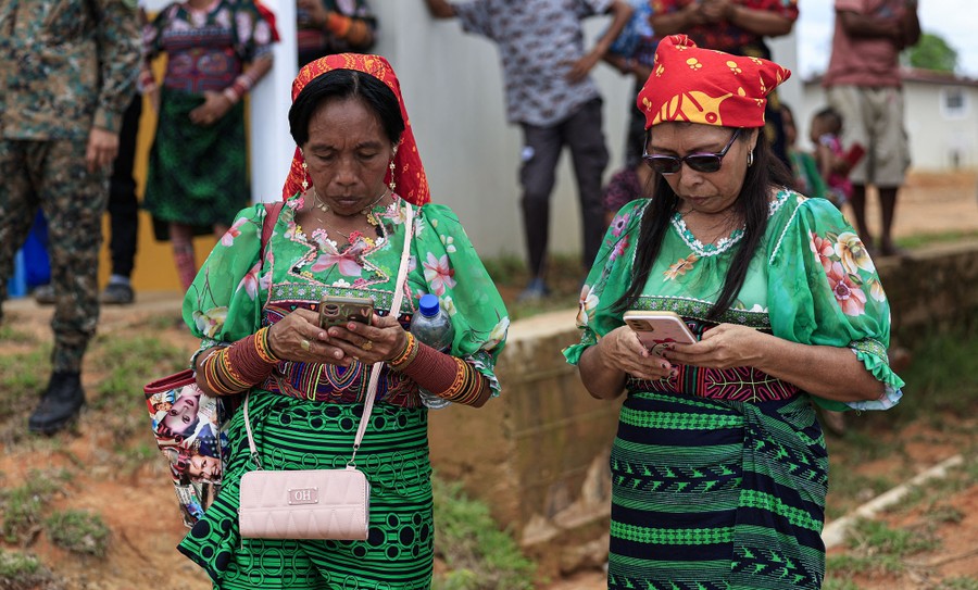 Two women in green patterned dresses check their mobile devices.