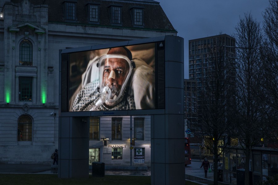 A lighted billboard displays a man in a hospital bed wearing a respiratory mask.