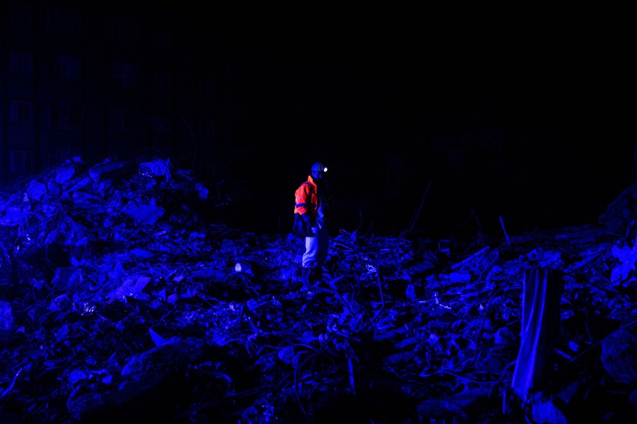 An emergency-service worker stands atop a pile of rubble at night.