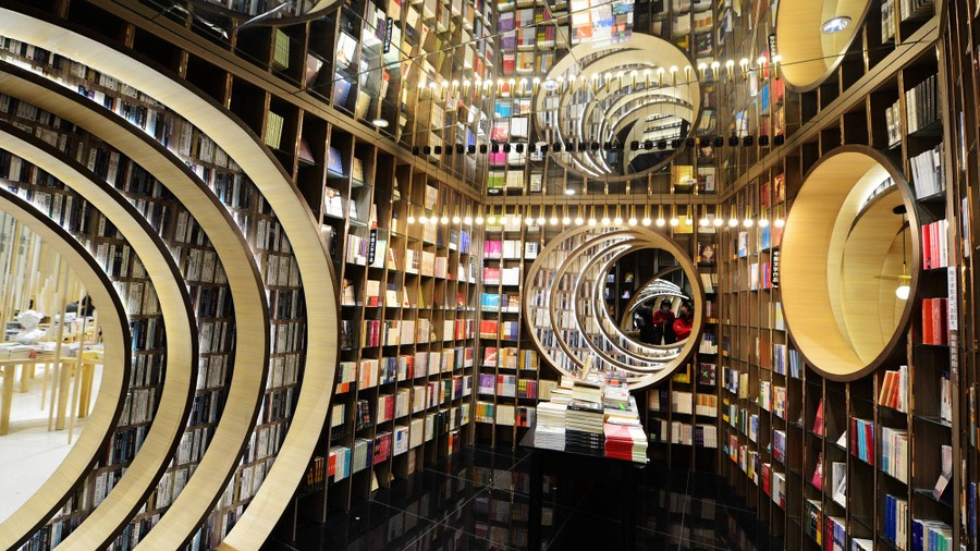 The interior of a bookstore, with many floor-to-ceiling bookshelves, a mirrored ceiling, and circular cutouts in the walls