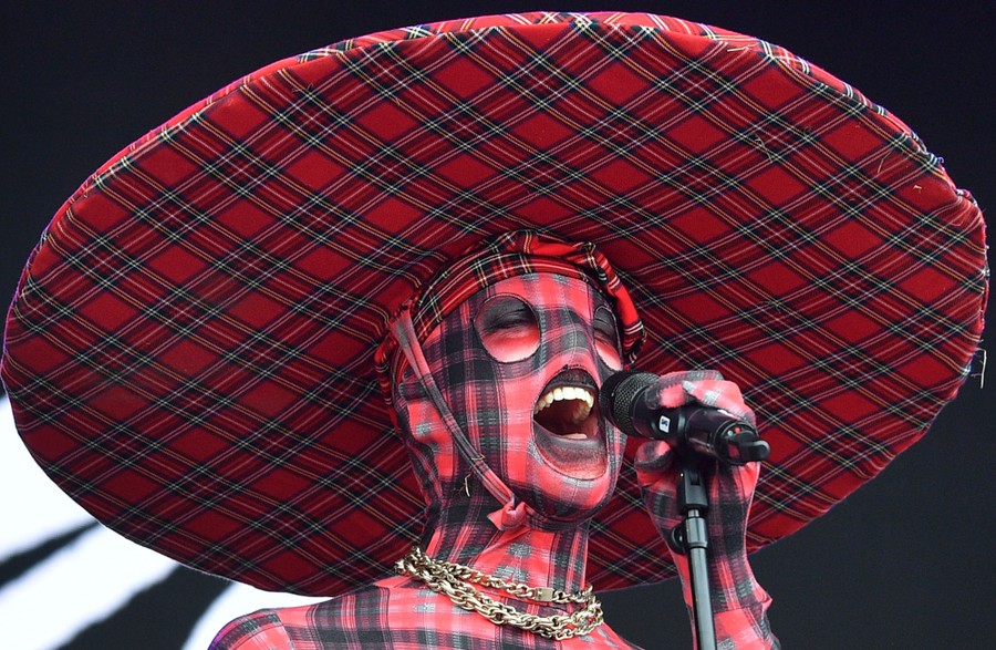 A performer sings while wearing a hat and mask made of plaid fabric.