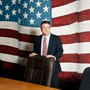 Photo of a man standing behind a desk chair against a wall painted with a large mural of the American flag