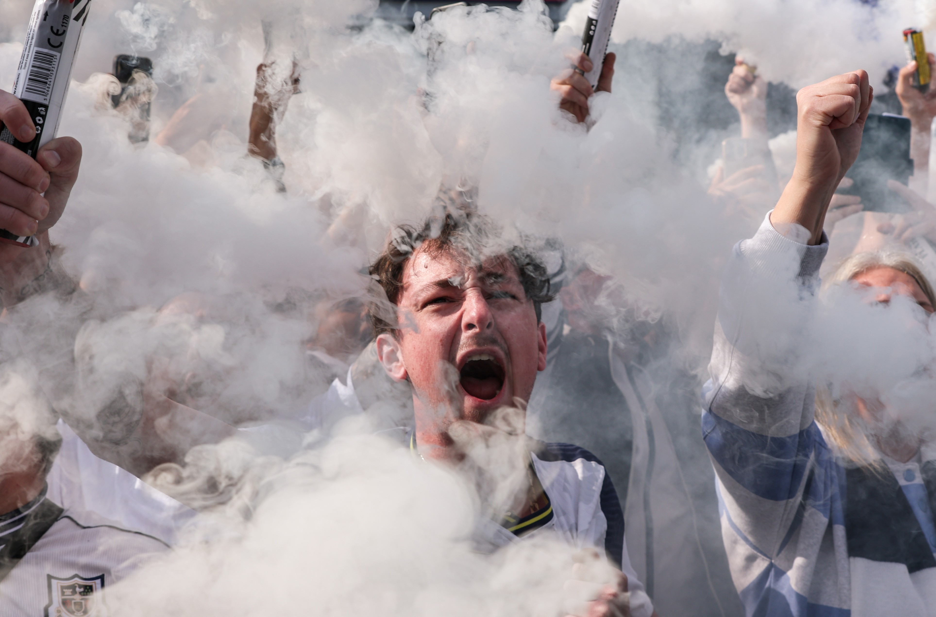 Soccer fans cheer, surrounded by smoke from flares.