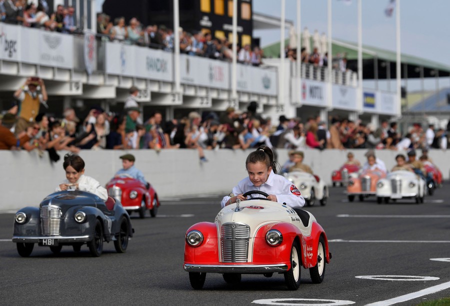 Children race on a race track, driving small replica pedal cars.