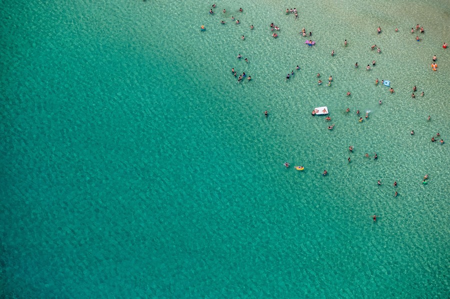 An aerial view of blue-green water, and several dozen swimmers