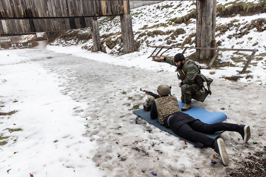 An instructor works with a person who lies prone, holding a rifle, aiming at targets on a rage.