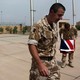 An Iraqi policeman walks past two British military officers, one folding the Union Jack.