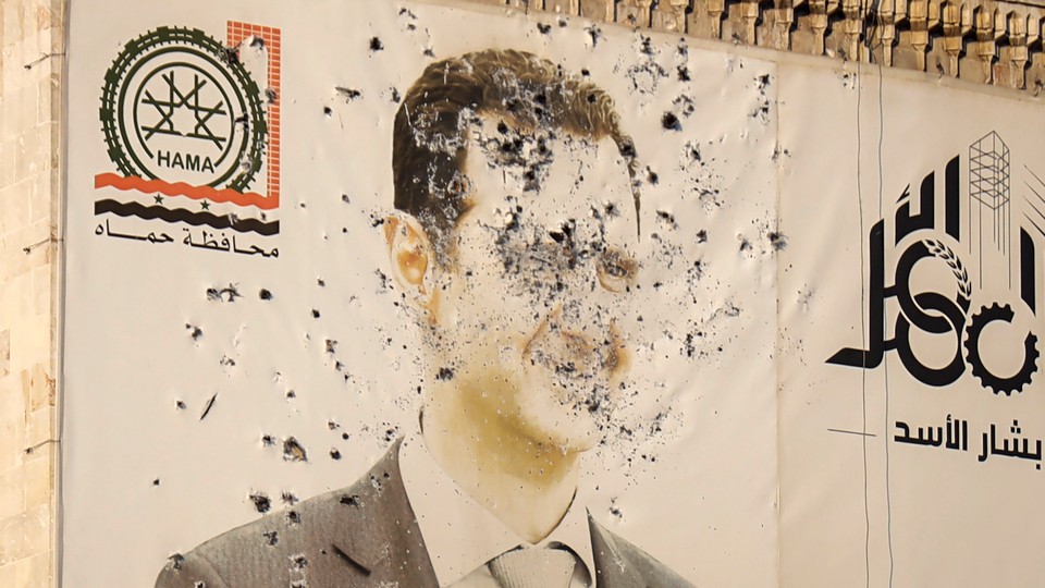 Photograph of a banner hung on a building depicting Syrian President Bashar al-Assad, riddled with bullet holes.