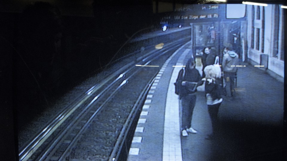 Grainy CCTV footage shows people standing at a train station.