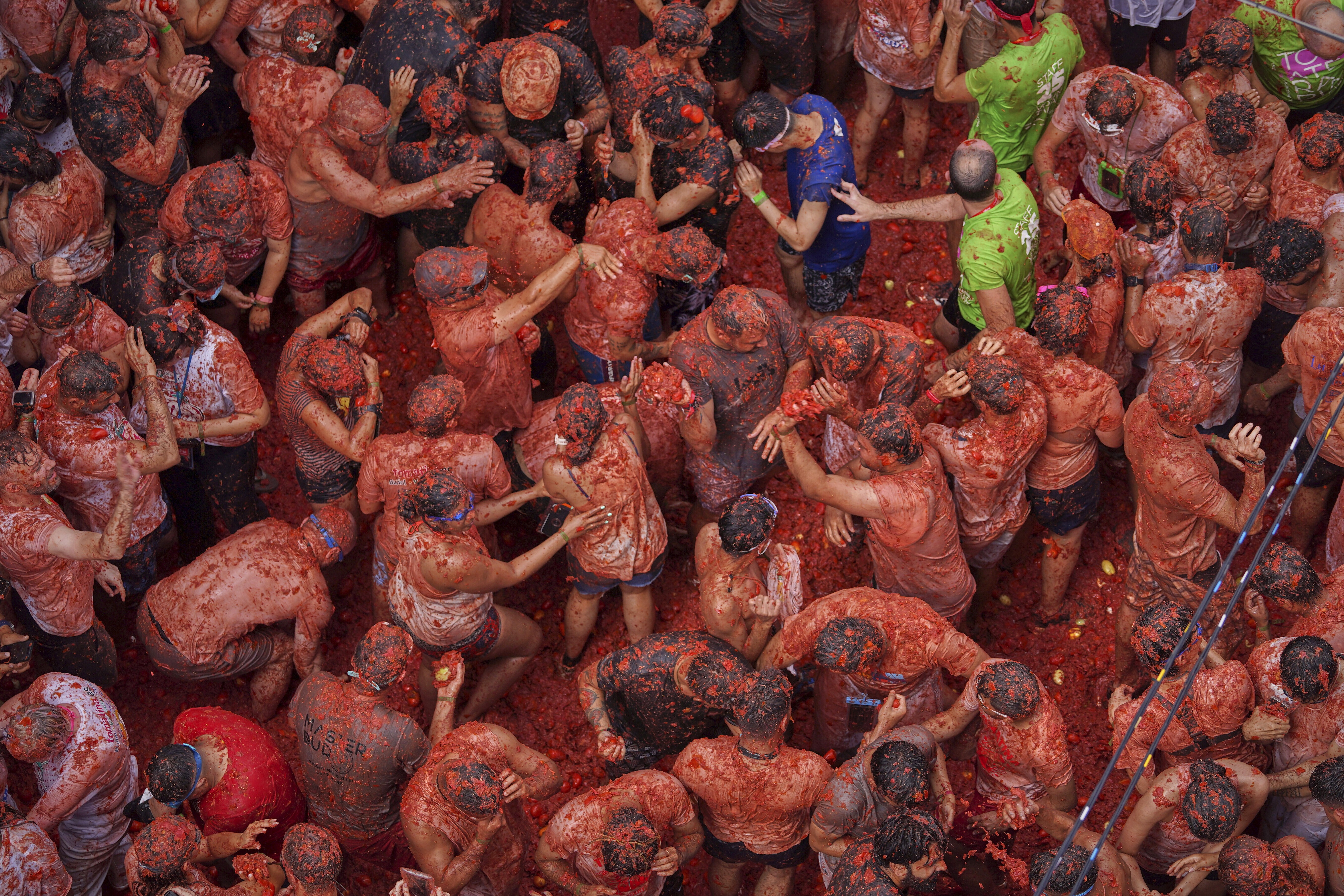 An elevated view of a large crowd of people completely covered in bits of tomato during a food-fight festival.