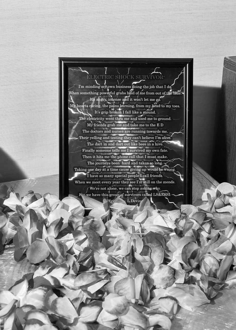 black-and-white photo of framed long poem in white text on dark background with lightning bolts, with flowers in foreground