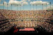 A sports stadium filled with people. In the center of the field, there is an American flag.