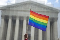 A hand holding a rainbow flag outside of the Supreme Court