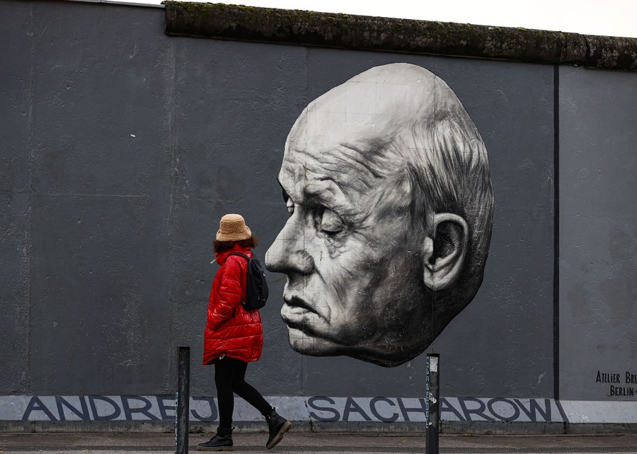 A person walks past a large portrait painted on a remnant of the Berlin Wall.