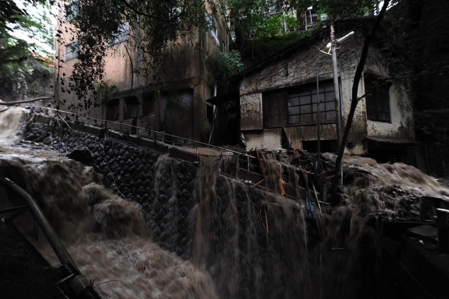 Water flows along streets and sidewalks, among debris in a hillside neighborhood.