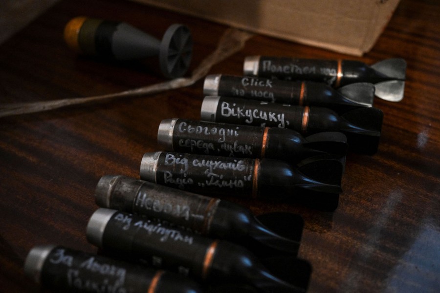 Eight or nine small cylindrical bombs with handwritten messages on them sit on a desktop.