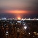 A photograph of Kyiv's skyline, in the dsitance and in the dark, lit up with ballistic missiles
