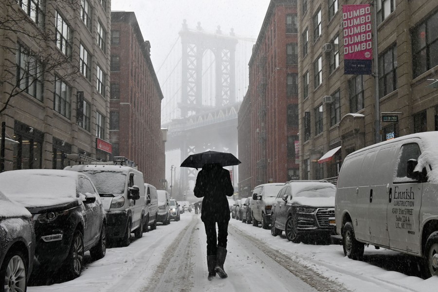 A man with an umbrella walks through a snowy street in New York City.